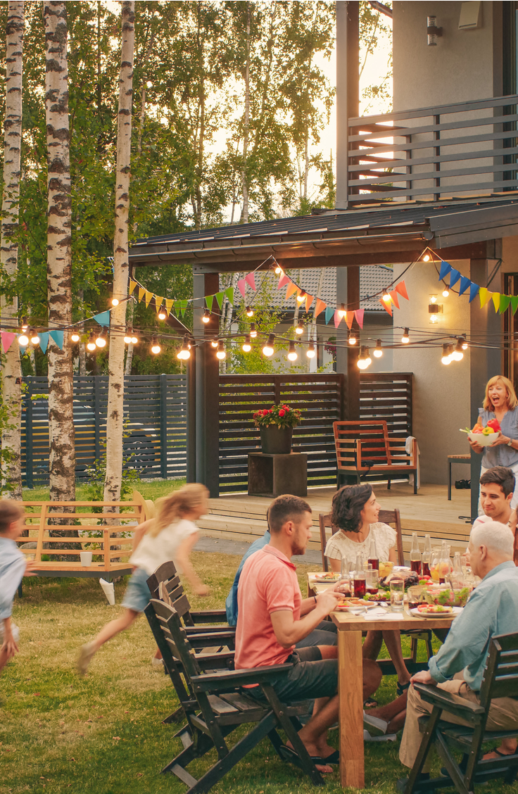 Family eating dinner on table in backyard. Backyard projects include covered deck and bench.

